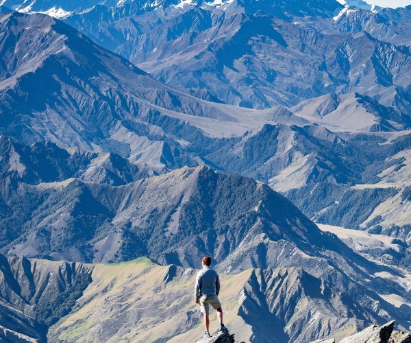 A man standing on a mountain peak overlooking a range of mountains